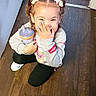 Lorelai is registered to the contest to win money with this photo: child, girl, toddler, hair_bows, sippy_cup, sweatshirt, leggings, sneakers, wood_floor, indoors, crouching, smiling, happy, cute, playful, funny, home, person, face, expression