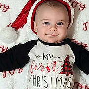 Emmett is registered to the contest to win money with this photo: baby, infant, smile, face, santa_hat, christmas, holiday, festive, red, white, black, shirt, blanket, lying_down, cute, child, portrait, happy, celebration, indoors