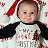 baby, black, blanket, celebration, child, christmas, cute, face, festive, happy, holiday, indoors, infant, lying_down, portrait, red, santa_hat, shirt, smile, white