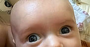 Braxton joined the competition — help win amazing prizes! baby, infant, child, portrait, face, eyes, wide_eyed, smiling, close_up, indoor, blanket, bed, cozy, warm_lighting, clothing, brown_clothing, head, bald, reclining, photography