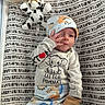 Braxton is registered to the contest to win money with this photo: newborn, baby, infant, child, portrait, lying_down, sleepwear, hat, mittens, pacifier, plush_toy, cow_toy, changing_mat, nursery, baby_supplies, patterned_blanket, elephant, clothing, face, indoor