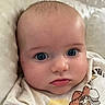 Braxton joined the competition — help win amazing prizes! baby, infant, child, portrait, close_up, face, eyes, wide_eyed, looking_at_camera, indoors, blanket, bedding, clothing, white_outfit, cartoon, printed_shirt, cozy, head, serious_expression, photography