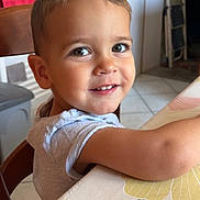 Léo participe au concours pour gagner de l'argent avec cette photo : child, toddler, smiling, face, eyes, table, chair, indoor, hair, clothing, arm, tablecloth, pattern, leaf, kitchen, tile_floor, door, furniture, person, happy