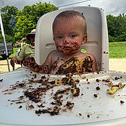 Gypsy is registered to the contest to win money with this photo: cake, child, chocolate, dirt, expressionless, face, food, greenery, hat, highchair, man, messy, nature, outdoor, person, seat, sky, summer, table, toddler