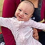 baby, child, smiling, face, person, holding, clothing, pink_outfit, floral_pattern, arm, adult, closeup, portrait, happy, cute, infant, skin, eyes, head, warmth