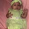 baby, infant, child, portrait, lying_down, pink_blanket, green_outfit, headband, bow, flower, dress, onesie, smiling, face, hands, fist, indoor, bedding, fashion, photography