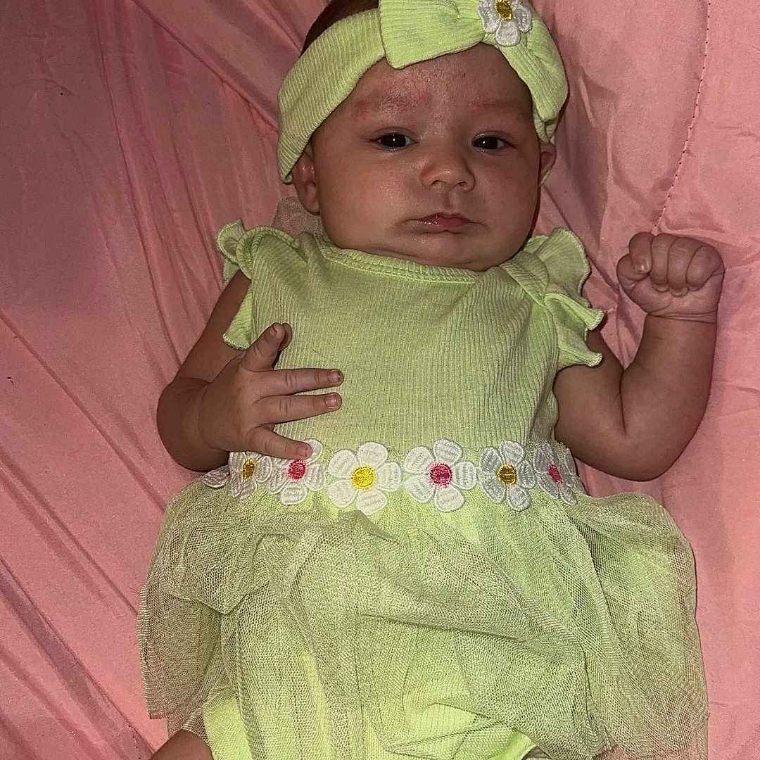 Leah joined the competition — help win amazing prizes! baby, infant, child, portrait, lying_down, pink_blanket, green_outfit, headband, bow, flower, dress, onesie, smiling, face, hands, fist, indoor, bedding, fashion, photography
