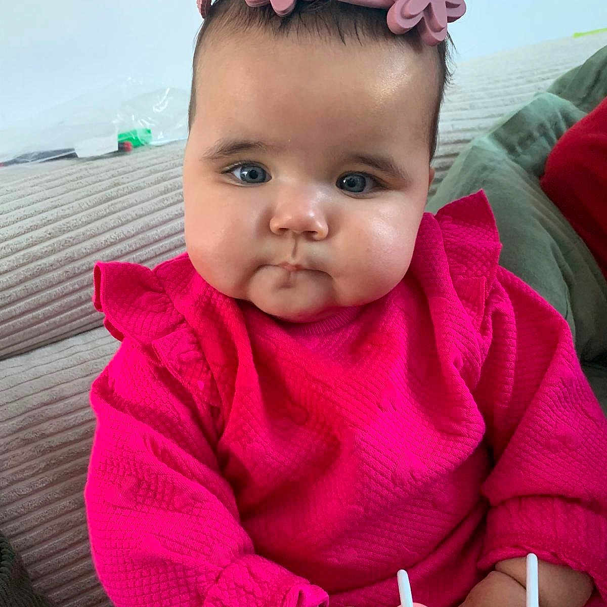 Ella a rejoint le concours — aidez-le/la à gagner de superbes lots ! baby, child, infant, pink_clothing, headband, flower_headband, toy, couch, indoor, portrait, cute, chubby_cheeks, hands, face, blue_eyes, curious, sitting, soft_texture, striped_couch, casual