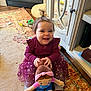 toddler, child, smiling, toy, doll, dress, hair_bow, socks, carpet, indoor, living_room, cabinet, wood_floor, happy, play, cute, person, furniture, colorful, cozy