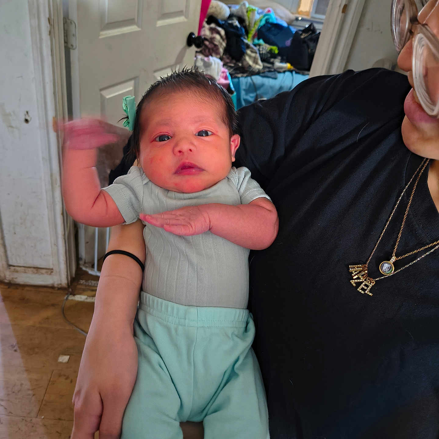 Heyzel is registered to the contest to win money with this photo: baby, black_shirt, casual, clothing, door, face, floor, furniture, glasses, hand, holding, indoor, infant, mint_pants, motion_blur, necklace, pacifier, person, room, window