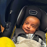 Desi is registered to the contest to win money with this photo: baby, car_seat, evenflo, blanket, smile, infant, child, seatbelt, face, head, clothing, fabric, safety, portrait, indoor, closeup, person, baby_clothes, soft_light, yellow_object