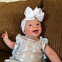 baby, child, smiling, blue_eyes, white_bow, headband, dress, floral_pattern, ruffles, sitting, couch, brown_couch, indoor, happy, cute, portrait, infant, face, skin, person