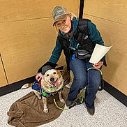 Kai joined the competition — help win amazing prizes! blanket, cap, casual_clothing, dog, floor, graduation_cap, hand, happy, indoor, jacket, jeans, leash, leash_handle, paper, pet, seated, smile, tongue_out, wall, woman