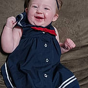 Vivianne is registered to the contest to win money with this photo: baby, child, smiling, dress, headband, blue, red_bow, sitting, couch, indoor, happy, cute, person, legs, tights, infant, cheerful, face, portrait, clothing