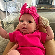 Irelynn joined the competition — help win amazing prizes! baby, infant, pink_clothing, headband, mittens, person, indoor, living_room, fireplace, baby_swing, carpet, couch, hand, legs, curious, wide_eyes, seated, cozy, home, soft_lighting