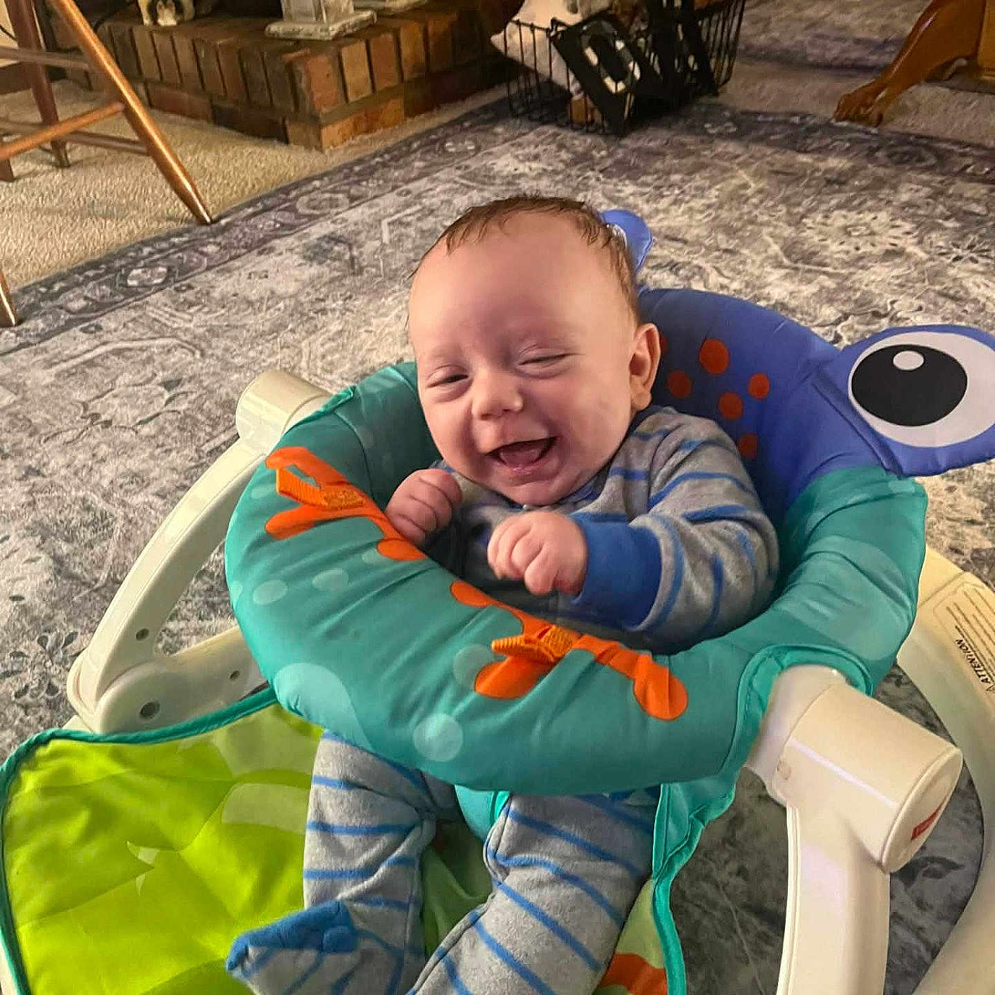 Tracyn is registered to the contest to win money with this photo: baby, baby_seat, carpet, cheeks, cozy, fireplace, furniture, hands, happy, home, indoor, infant, laughing, onesie, portrait, rug, smiling, socks, striped_clothing, toy