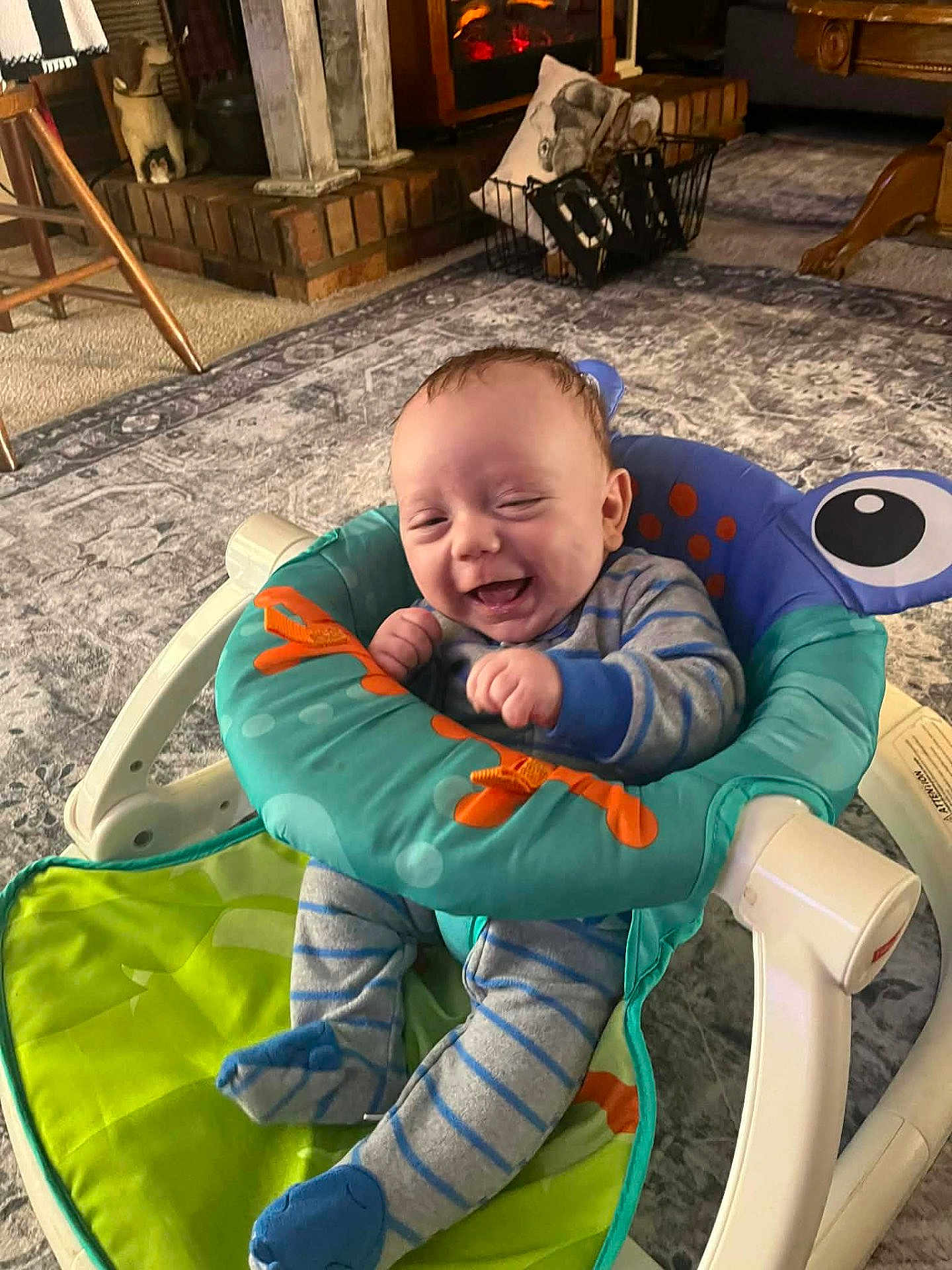 Tracyn is registered to the contest to win money with this photo: baby, infant, smiling, laughing, baby_seat, onesie, striped_clothing, socks, hands, cheeks, carpet, rug, indoor, home, fireplace, furniture, cozy, toy, happy, portrait