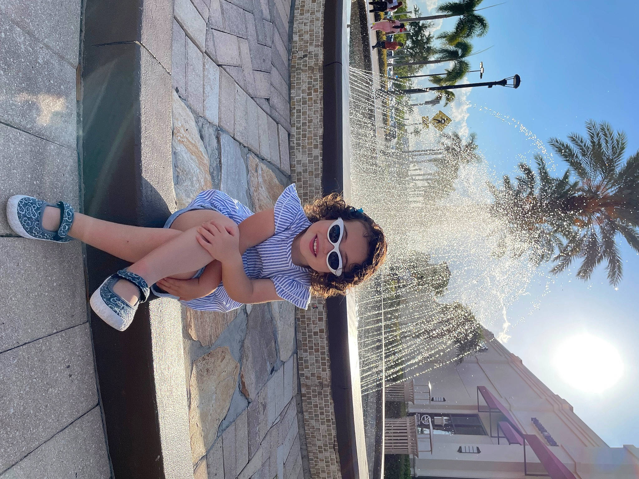 Rachel is registered to the contest to win money with this photo: building, calf, city, daytime, electric_blue, eyewear, facade, foot, fun, human_leg, joy, leisure, person, sandal, shorts, sky, smile, sneakers, thigh, tree