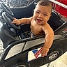 baby, black, cart, child, face, floor, hand, happy, indoor, infant, person, red, retail, seat, shirtless, shopping_cart, smiling, steering_wheel, store, toy_car