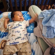 David joined the competition — help win amazing prizes! child, baby, infant, crib, blanket, pillow, onesie, shorts, socks, wooden_crib, bedding, shark_pattern, blue_color, remote_control, lying_down, raised_arm, face, portrait, nursery, teddy_pattern