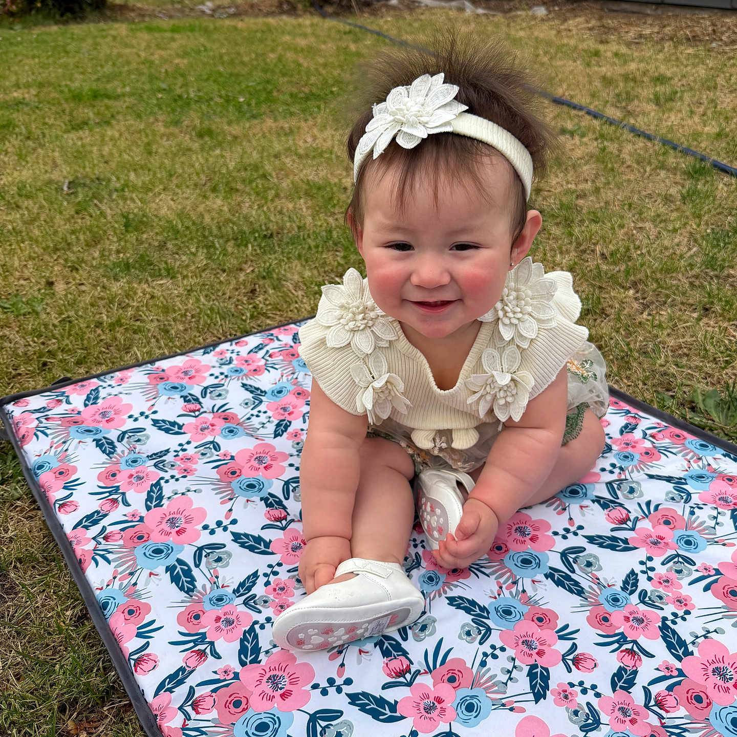 Kamila is registered to the contest to win money with this photo: baby, child, smiling, outdoor, grass, flower_mat, headband, white_clothing, cute, happy, sitting, person, young_child, lawn, garden, shoes, flower_pattern, playtime, nature, portrait
