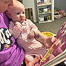 baby, child, reading, book, pink_onesie, purple_shirt, tattoo, butterfly_tattoo, indoor, carpet, shelf, toys, adult, holding, curious, face, person, home, cozy, engaged