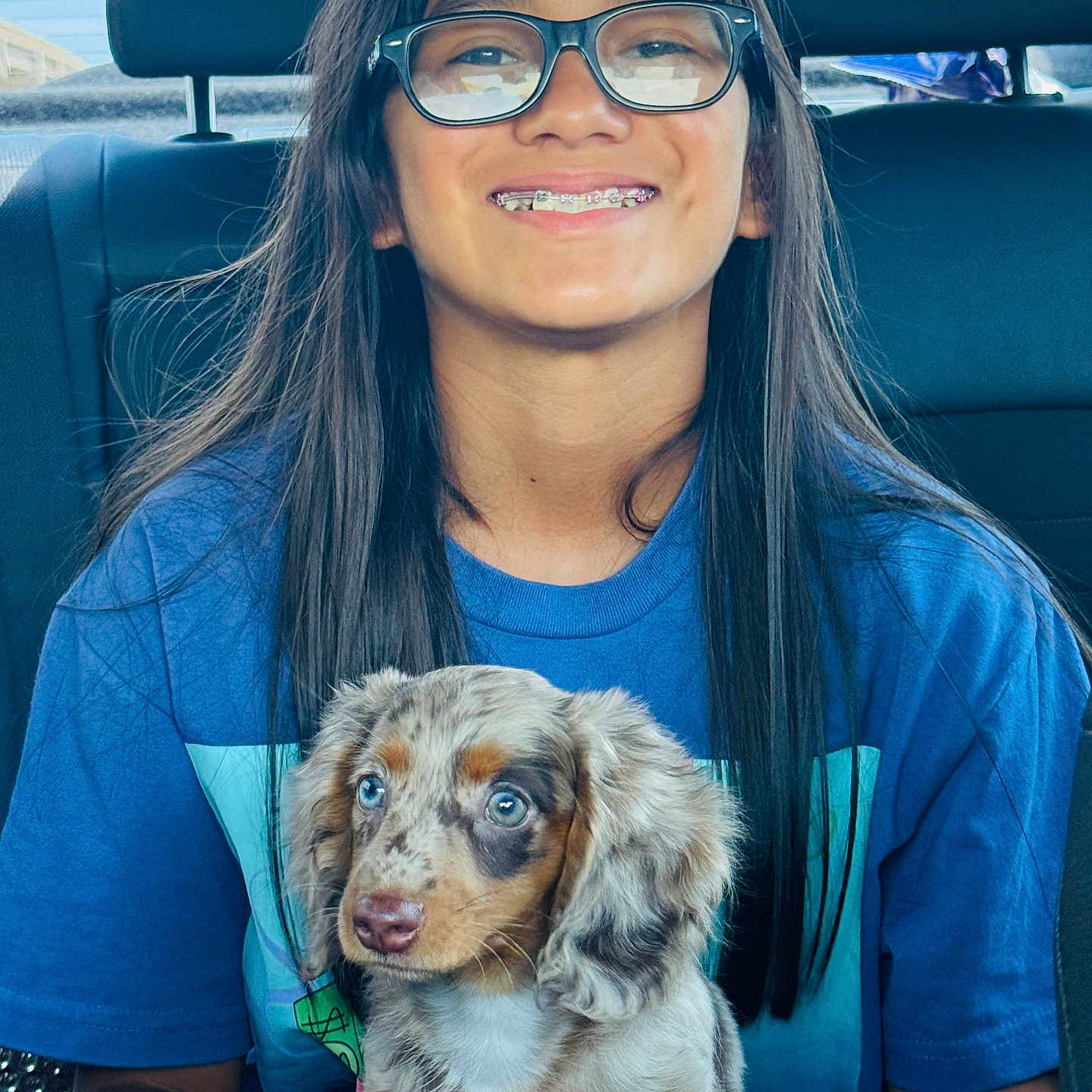 Piper Morones joined the competition — help win amazing prizes! animal, blue_shirt, braces, car_interior, child, cute, daylight, dog, glasses, happy, holding, long_hair, person, pet, puppy, seat, sitting, smile, window, young