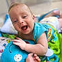 baby, smiling, play_mat, toy, teething_ring, infant, happy, child, blue_clothing, colorful, cute, closeup, hand, face, lying_down, indoors, soft_toys, cheerful, skin, expression