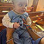 baby, child, infant, blue_suit, striped_clothing, hands, tattoo, bracelet, church, wooden_pews, sunlight, indoor, toy, curious, holding, person, face, eyes, clothing, seated