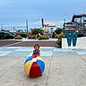 child, toddler, smiling, outdoor, amusement_park, water_park, beach_ball, colorful_ball, playground, vacation, summer, pavement, street, sign, water_slide, buildings, vehicles, landscaping, portrait, daylight
