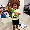Armani is registered to the contest to win money with this photo: child, toddler, cowboy, cowboy_hat, boots, lasso, toy, playroom, indoors, living_room, bedroom, smiling, curly_hair, standing, portrait, clothing, shorts, wooden_floor, furniture, playful