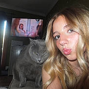 Ash is registered to the contest to win money with this photo: blonde_hair, cabinet, casual, cat, chair, curtains, expression, floor, furniture, gray_cat, home, indoor, living_room, long_hair, pet, portrait, puckered_lips, selfie, television, woman