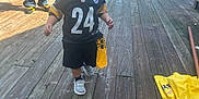 Lorenzo is registered to the contest to win money with this photo: child, toddler, football_jersey, face_paint, outdoor, wooden_deck, adult, sports_fan, casual_clothing, daylight, chairs, table, string_lights, smiling, person, walking, yellow, black, shoes, hat
