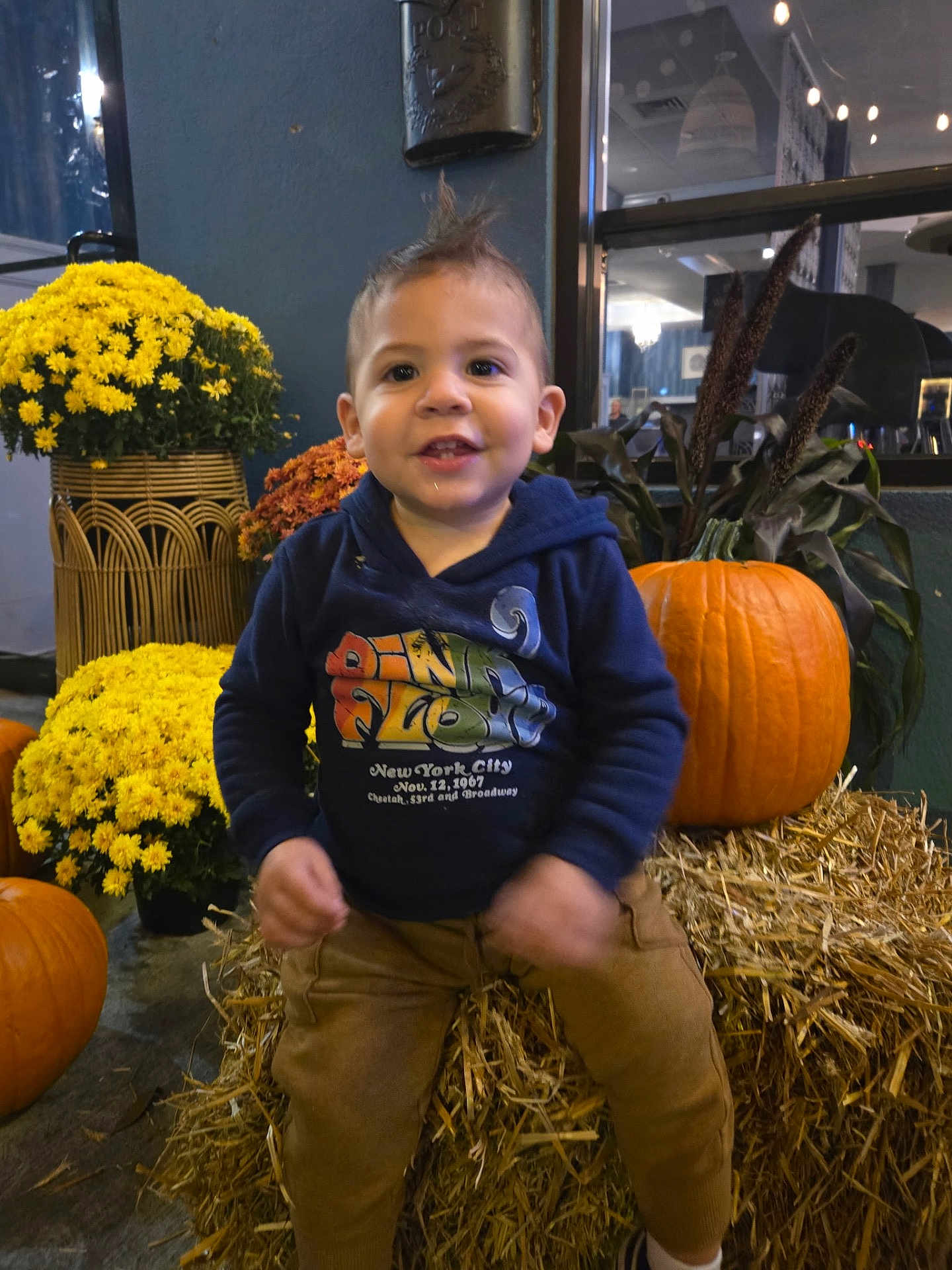 Lorenzo joined the competition — help win amazing prizes! toddler, child, pumpkin, hay, flowers, autumn, smiling, blue_hoodie, brown_pants, indoors, decoration, festival, yellow_flowers, orange_pumpkin, cute, happy, portrait, small_child, fall, casual_clothing