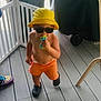 Lorenzo is registered to the contest to win money with this photo: toddler, child, yellow_hat, sunglasses, toy, orange_shorts, bare_chest, black_clogs, wooden_floor, indoor, baby, cute, standing, playful, summer, sunhat, footwear, diaper, accessory, fashion
