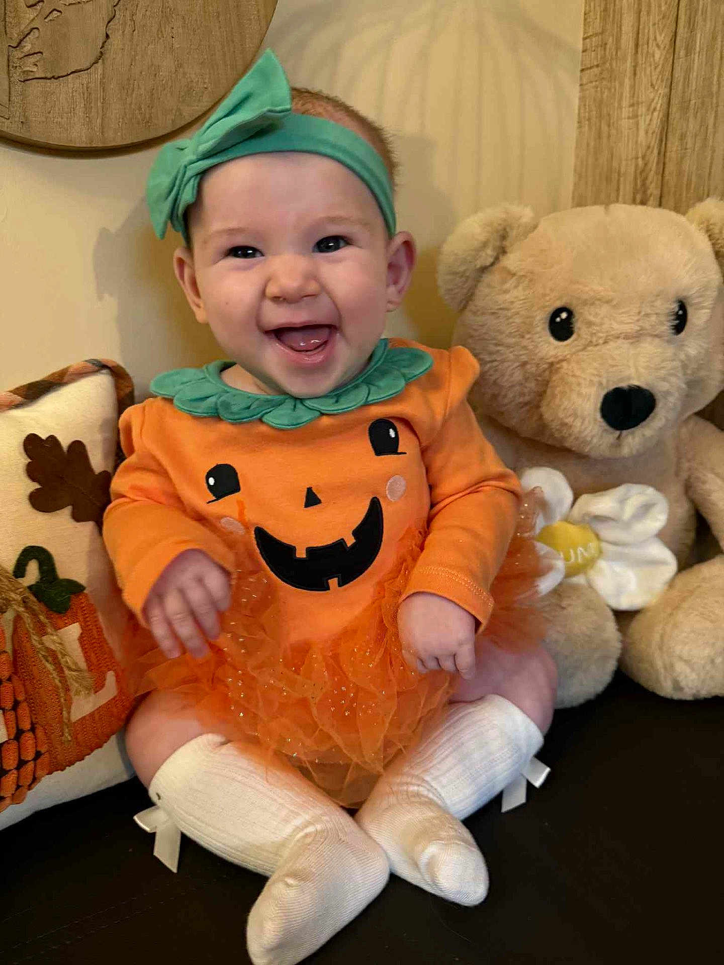 Leia joined the competition — help win amazing prizes! baby, child, smiling, pumpkin_outfit, headband, tutu, white_socks, teddy_bear, plush_toy, pillow, autumn, indoor, happy, cute, sitting, face, person, clothing, decor, festive