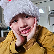 Eden a rejoint le concours — aidez-le/la à gagner de superbes lots ! child, smiling, face, hands, hat, santa_hat, yellow_sweater, indoor, portrait, close_up, happy, cute, casual_clothing, person, home, cozy, holiday, festive, expression, young