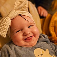Inaë participe au concours pour gagner de l'argent avec cette photo : baby, smiling, headwrap, cute, child, infant, clothing, portrait, happy, cozy, soft, yellow, grey, animal_print, seal, indoor, warm_lighting, cheeks, tongue, person