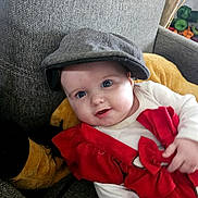 Inaë a rejoint le concours — aidez-le/la à gagner de superbes lots ! baby, blue_eyes, bow, cap, child, couch, cozy, cute, face, gray_fabric, hand, happy, indoor, infant, plush_toy, portrait, red_clothing, seated, smile, soft_lighting