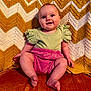 Lydia is registered to the contest to win money with this photo: baby, child, smiling, sitting, knit_blanket, zigzag_pattern, green_clothing, pink_shorts, barefoot, indoor, portrait, happy, cute, infant, soft_texture, cozy, warm_colors, face, person, candid