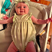 Lydia is registered to the contest to win money with this photo: baby, infant, headband, bow, smile, arms, clothing, seat, cushion, pacifier, baby_wipes, wood_floor, indoor, person, cute, happy, child, closeup, plush, relaxed