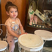 Aaliyah joined the competition — help win amazing prizes! child, girl, smiling, sitting, chair, table, pink_sneakers, wooden_background, vintage_display, glass_case, indoors, clothing, playful, cute, happy, person, legs, floor, furniture, hair