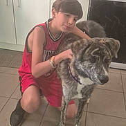 Heubert participe au concours pour gagner de l'argent avec cette photo : boy, child, dog, brindle_dog, pet, canine, hugging, sitting, indoors, kitchen, tile_floor, oven, cabinet, portrait, pet_owner, casual_clothing, red_shirt, sneakers, collar, family