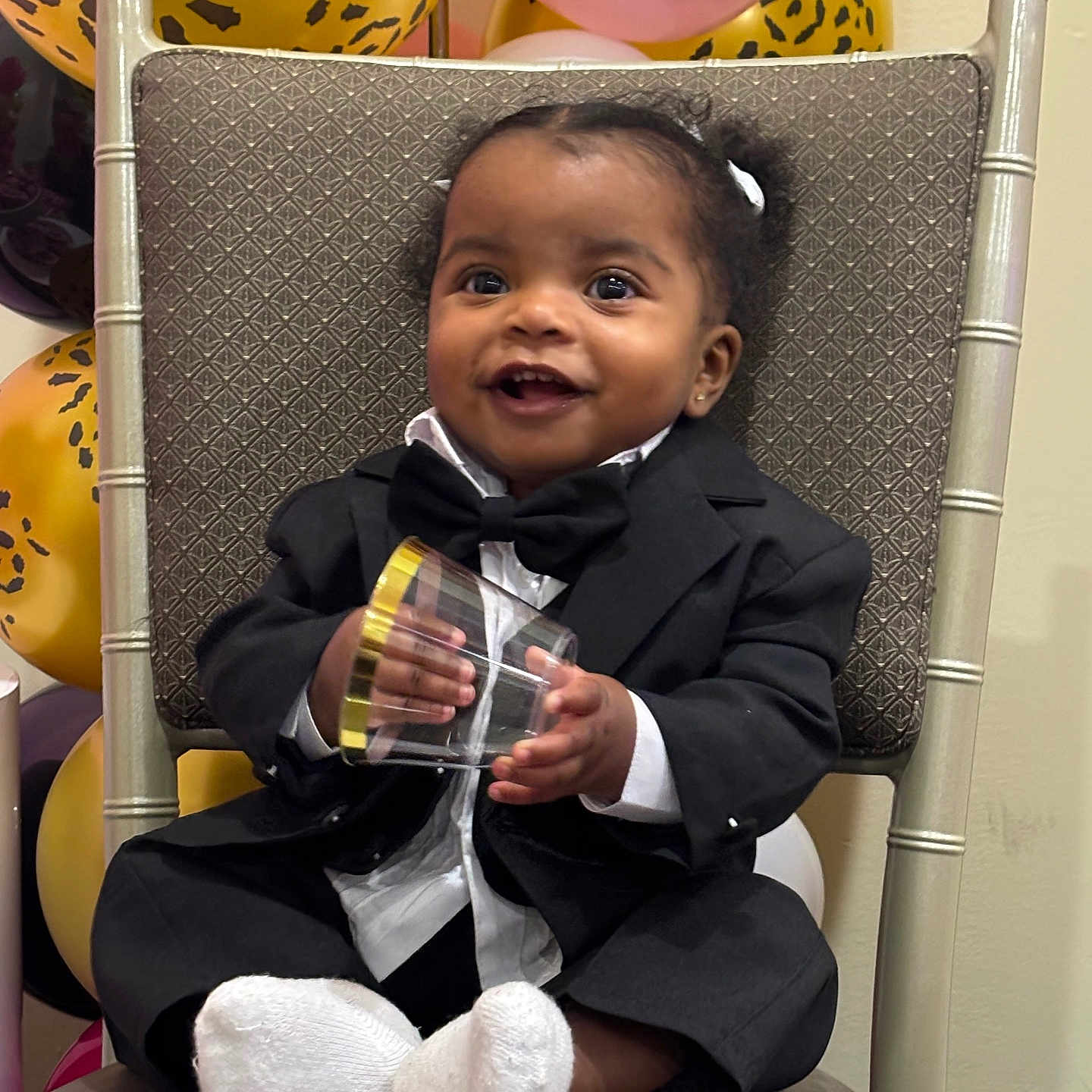 Alisia joined the competition — help win amazing prizes! baby, child, tuxedo, suit, bow_tie, chair, balloons, leopard_print, pink_balloon, smiling, happy, socks, indoor, celebration, party, cute, portrait, person, holding_object, festive