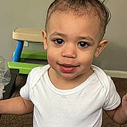 Grayson is registered to the contest to win money with this photo: toddler, child, smiling, white_shirt, indoor, carpet, furniture, toy, topknot, cute, young_child, portrait, person, happy, face, baby, standing, home, casual, curly_hair