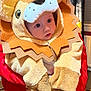 baby, child, lion_costume, plush, costume, indoors, person, red_jacket, face, cute, animal_costume, childrens_clothing, portrait, warm_clothing, home_interior, carpet, window_blinds, radiator, soft_toys, closeup