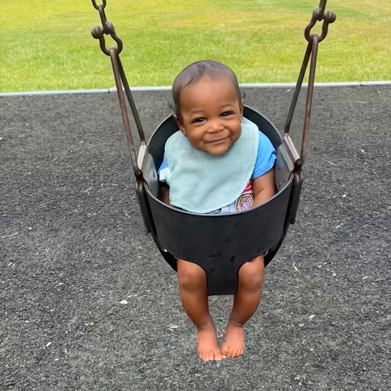 Zephaniah is registered to the contest to win money with this photo: baby, child, toddler, swing, playground, smiling, happy, portrait, outdoor, playground_surface, grass, bib, blue_shirt, barefoot, swing_chains, seated, infant, face, playtime, lawn
