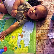 Noah is registered to the contest to win money with this photo: baby, child, play_mat, curious, indoors, carpet, colorful, light, shadow, infant, person, lying_down, young_child, casual_clothing, expression, floor, soft_surface, playtime, home, relaxed