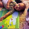 baby, child, play_mat, curious, indoors, carpet, colorful, light, shadow, infant, person, lying_down, young_child, casual_clothing, expression, floor, soft_surface, playtime, home, relaxed