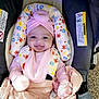 baby, car_seat, blanket, pink_clothing, headband, smiling, infant, face, child, cushion, fabric, soft, indoors, happy, portrait, cute, wrapped, seatbelt, person, cozy